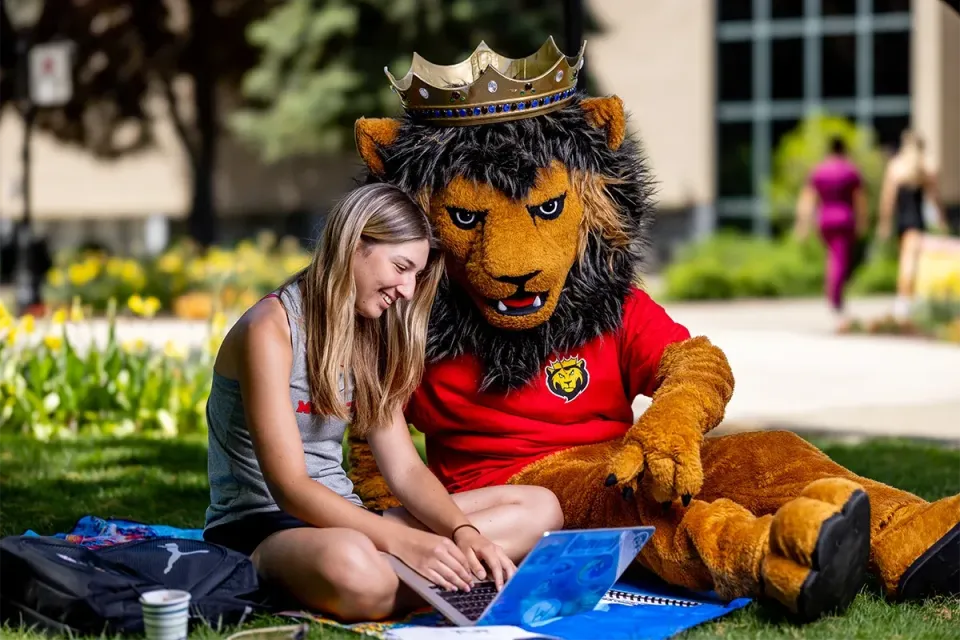 King's student sitting outdoors with Leo the lion mascot