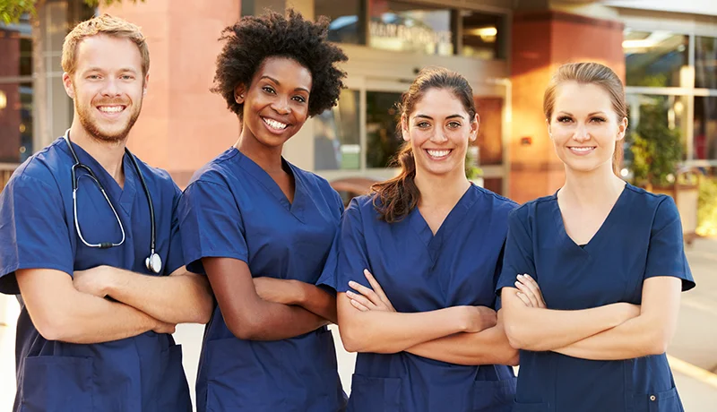nurses pose in front of a hospital in scrubs