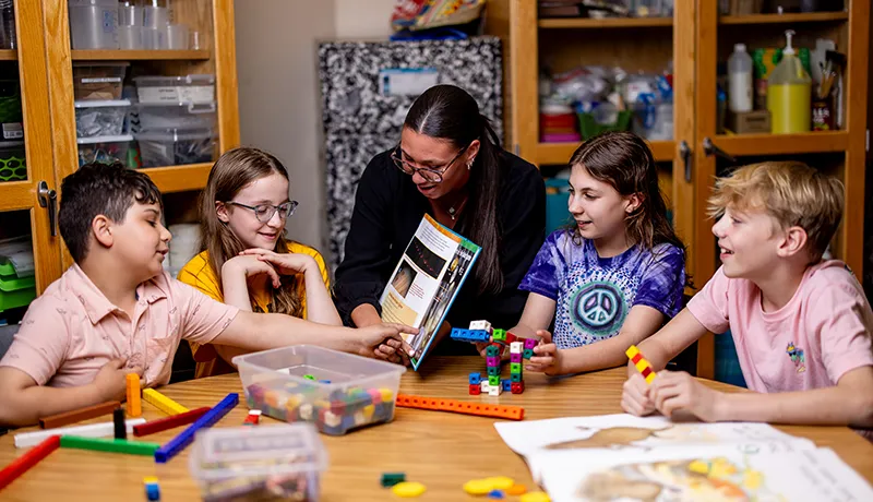 A teacher with a group of elementary students at a table