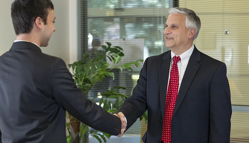 student shaking hands with an elderly man in a suit