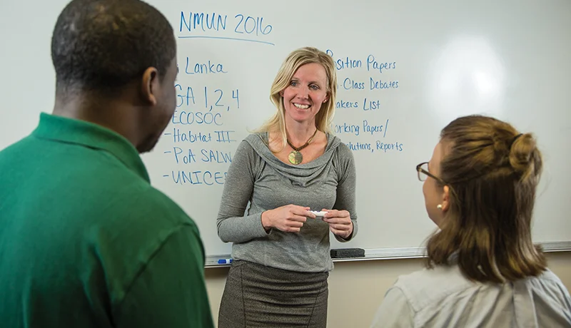 students and a professor talking in front of a whiteboard