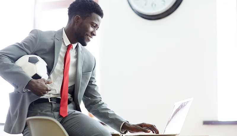 sports management degree student working on the computer while holding a soccer ball