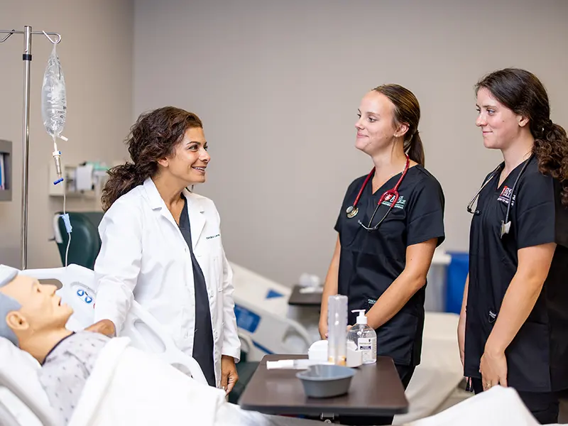 three nursing students next to a dummy in a hospital bed