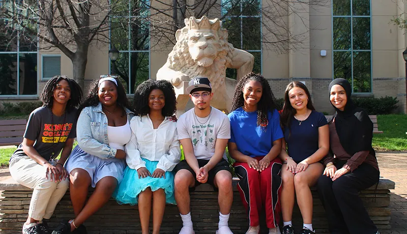multicultural students seated outdoors near a lion statue