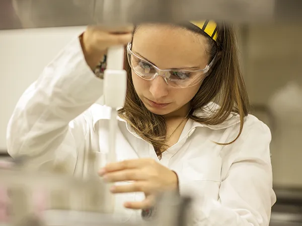 student in protective wear using a beaker and syringe