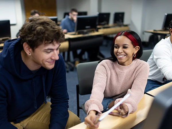 two students in a computer lab reading a printout