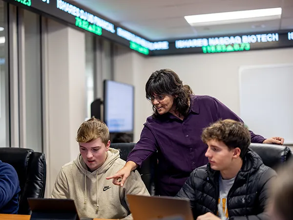 a professor with two students pointing at a laptop