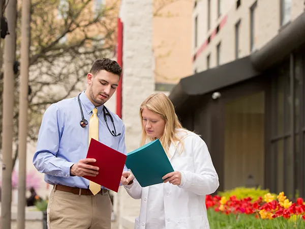a man in a dress shirt meeting with a woman in a labcoat outdoors