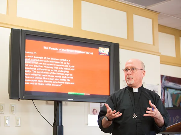 a catholic priest teaching a class in front of a monitor