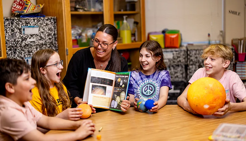 a teacher at a table with several elementary school-aged children