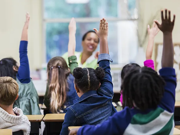 children raising their hands in a classroom