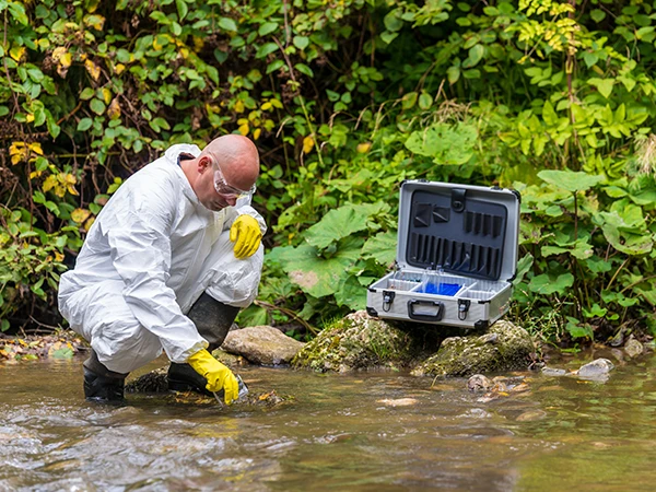 person collecting a water sample in a creek, partof environmental chemistry jobs