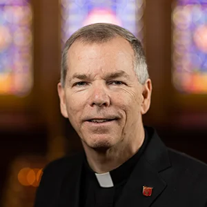 Portrait photo of Fr. Looney in front of stained glass windows.