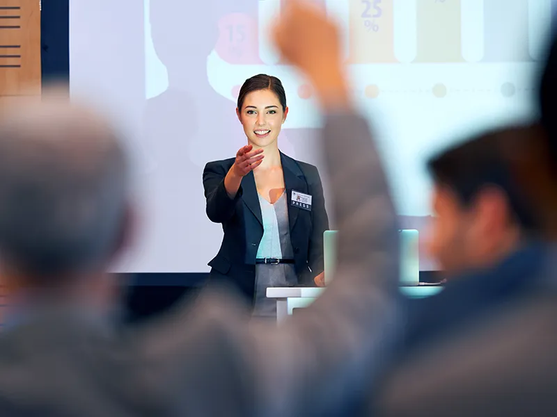 a presenter in a suit pointing to an audience