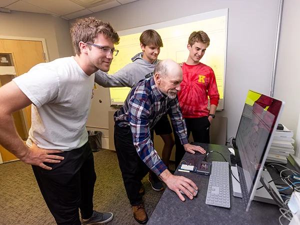 professor and students setting reviewing engineering plans on a computer