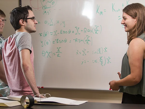 students standing in front of a white board with equations on it