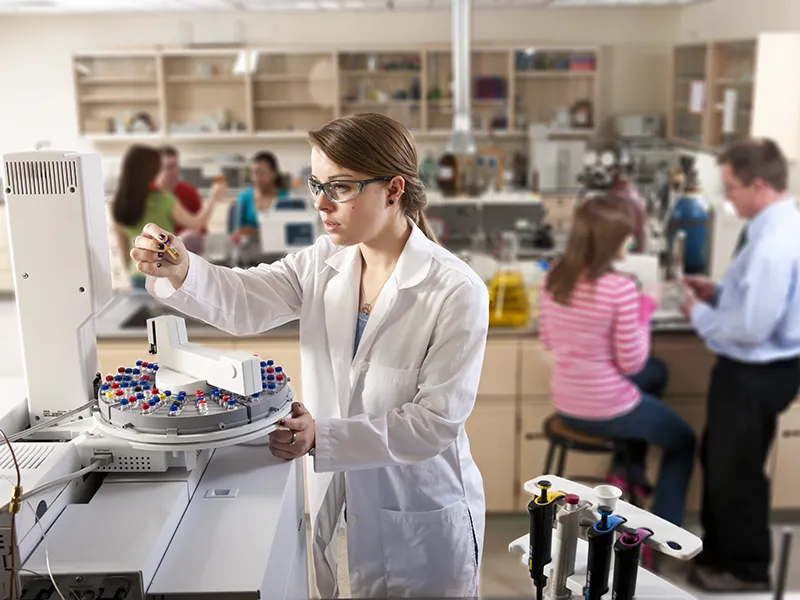 student in labcoat reading a beaker