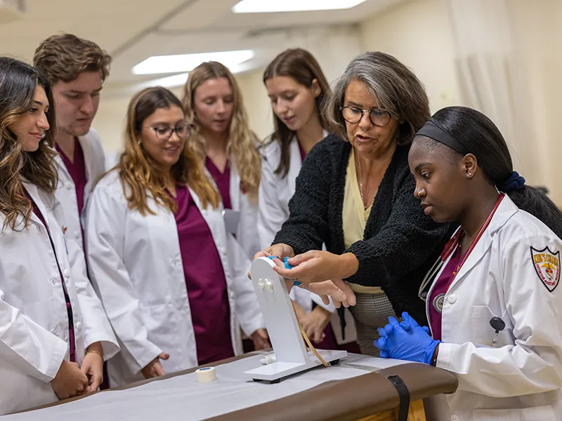 students in lab coats and medical scrubs talking to a professor