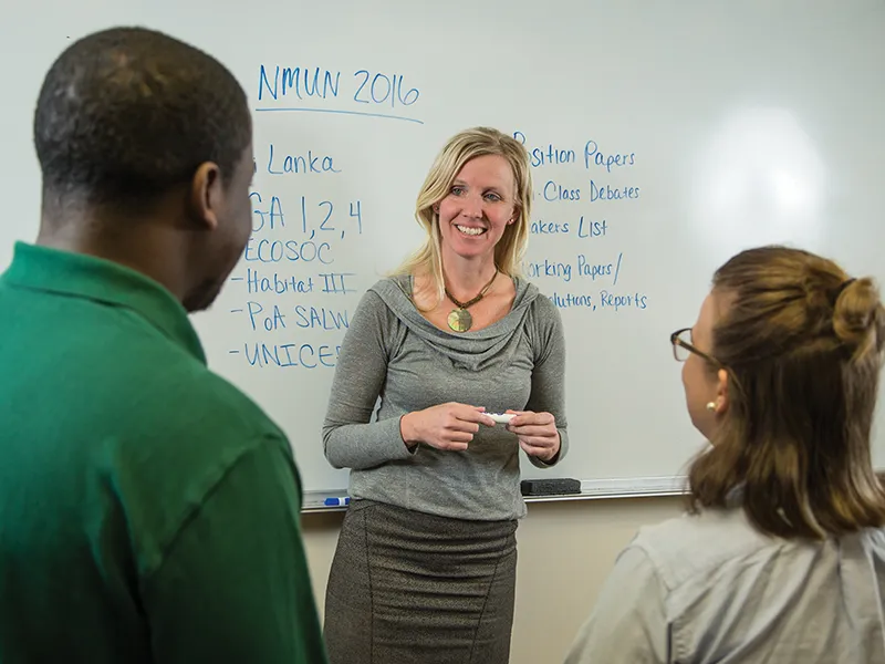 students talking to a professor in front of a whiteboard