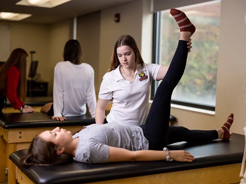 a student in a Polo shirt lifting a patient's leg