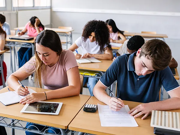 high school students writing at desks in a classroom