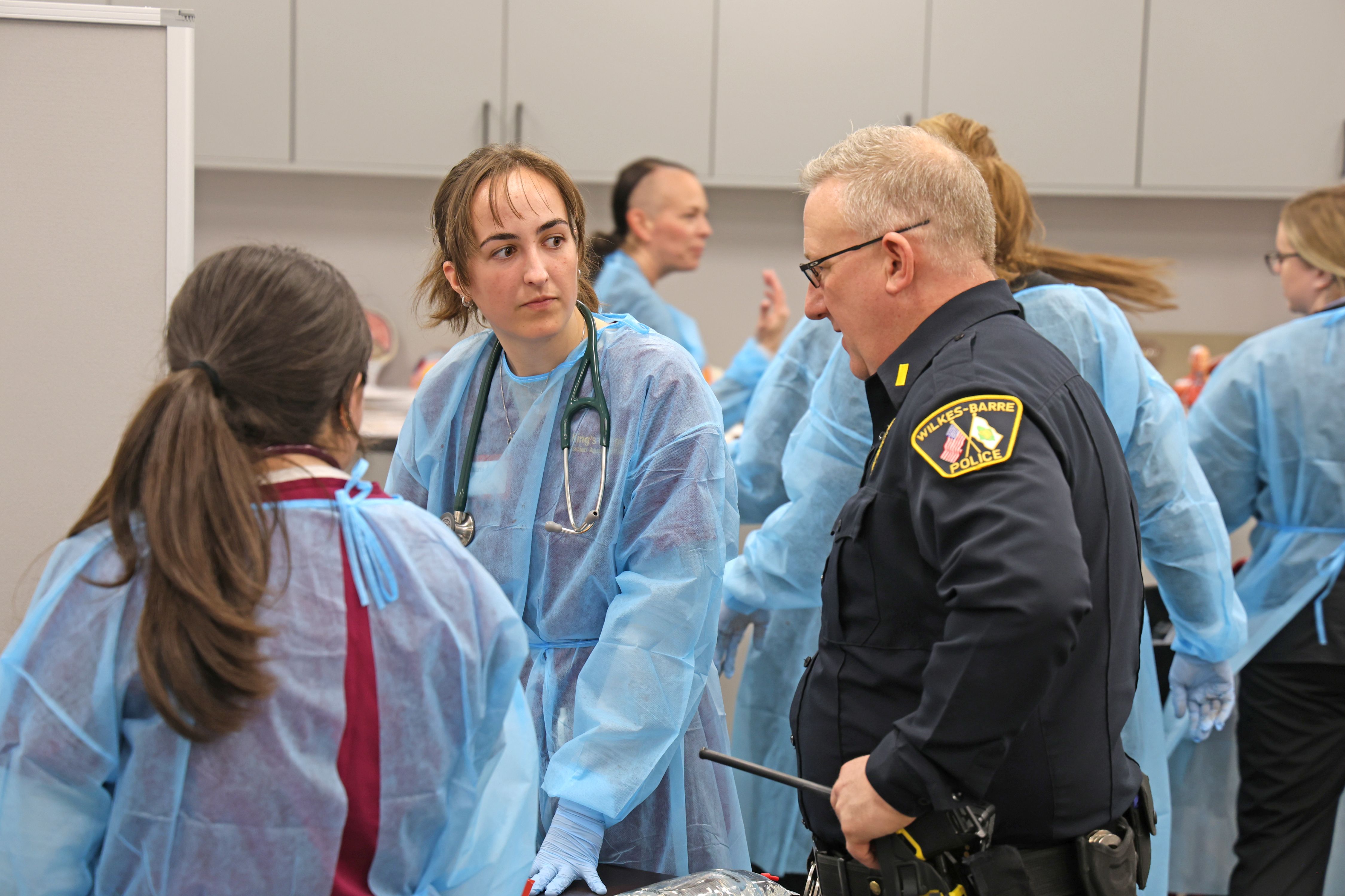 Physician assistant students Hailey D'Amato (facing camera) and Kelimarie Romero (back to camera) with Lt. Sheridan. Background: Jackie Murphy and Katie Stump, ABSN nursing students.