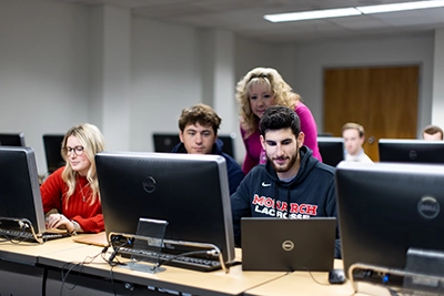 students interact with a professor in a computer lab.