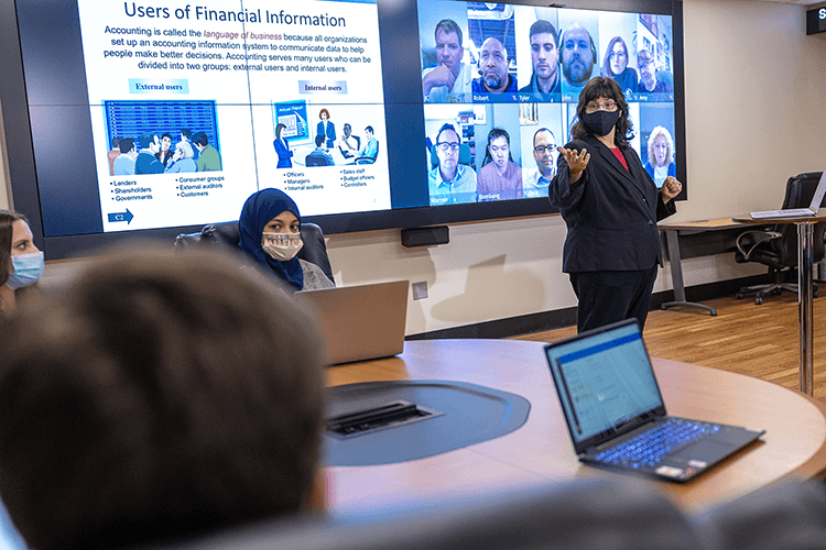 Accounting professor in professional attire engages with students during a lecture.