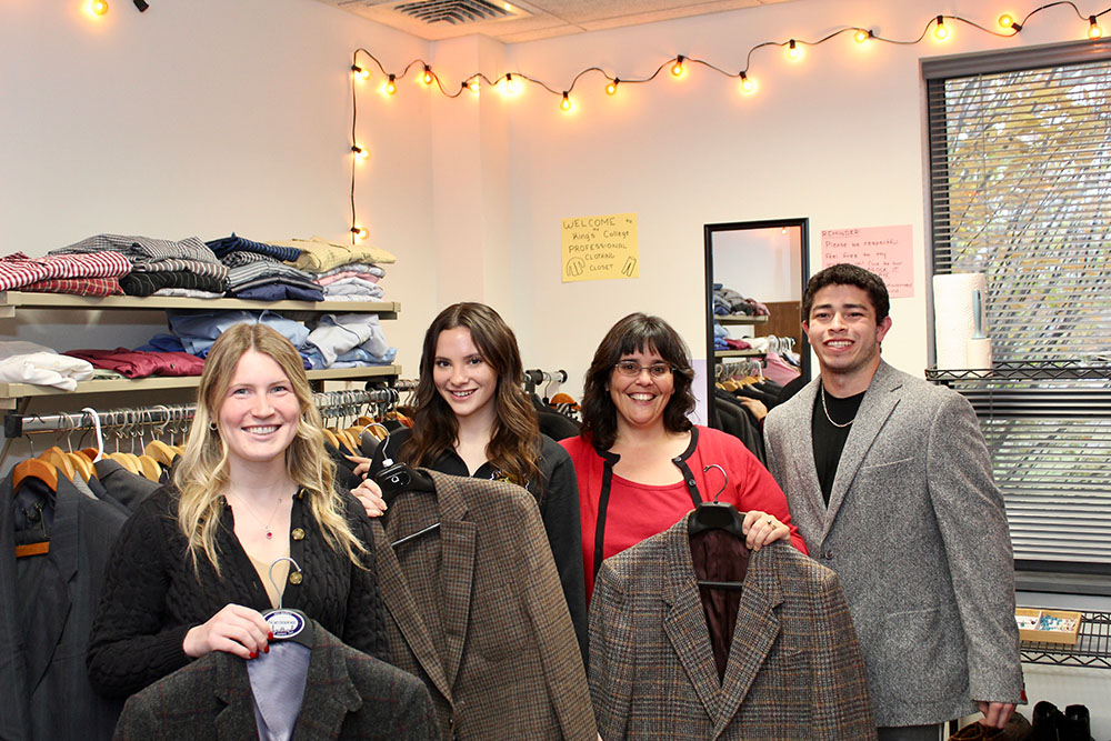 Students and faculty pose with suit jackets in a closet that provides formal clothing for students in need.