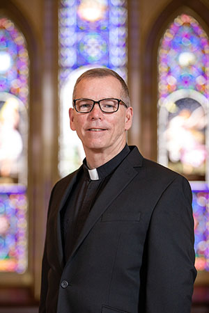 Portrait photo of Fr. Looney in front of stained glass windows.