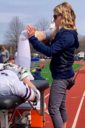 Kelsey helps an athlete stretch by lifting his leg.