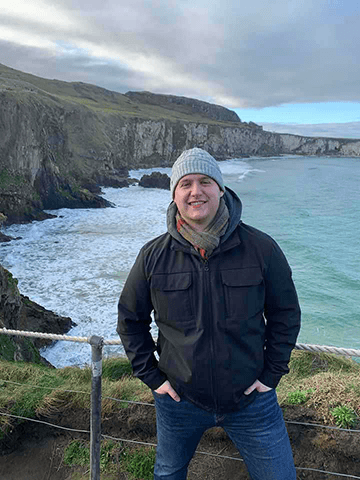 Jarett poses in front of a rocky coastline in Northern Ireland.